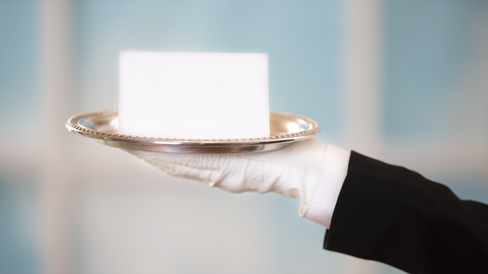 White gloved hand in black suit holds a blank notecard on a silver platter.