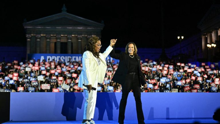 Oprah Winfrey and Kamala Harris hold hands in front of a crowd