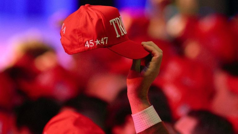 A Trump supporter holds a TRUMP hat that reads: 45 star 47