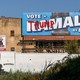 A “Vote Kamala” advertisement hangs defaced with “Trump” graffiti near a mural for fallen soldiers on Election Day in Philadelphia.