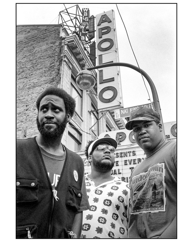 Three men dressed casually posing in front of a theater with the vertical sign APOLLO.