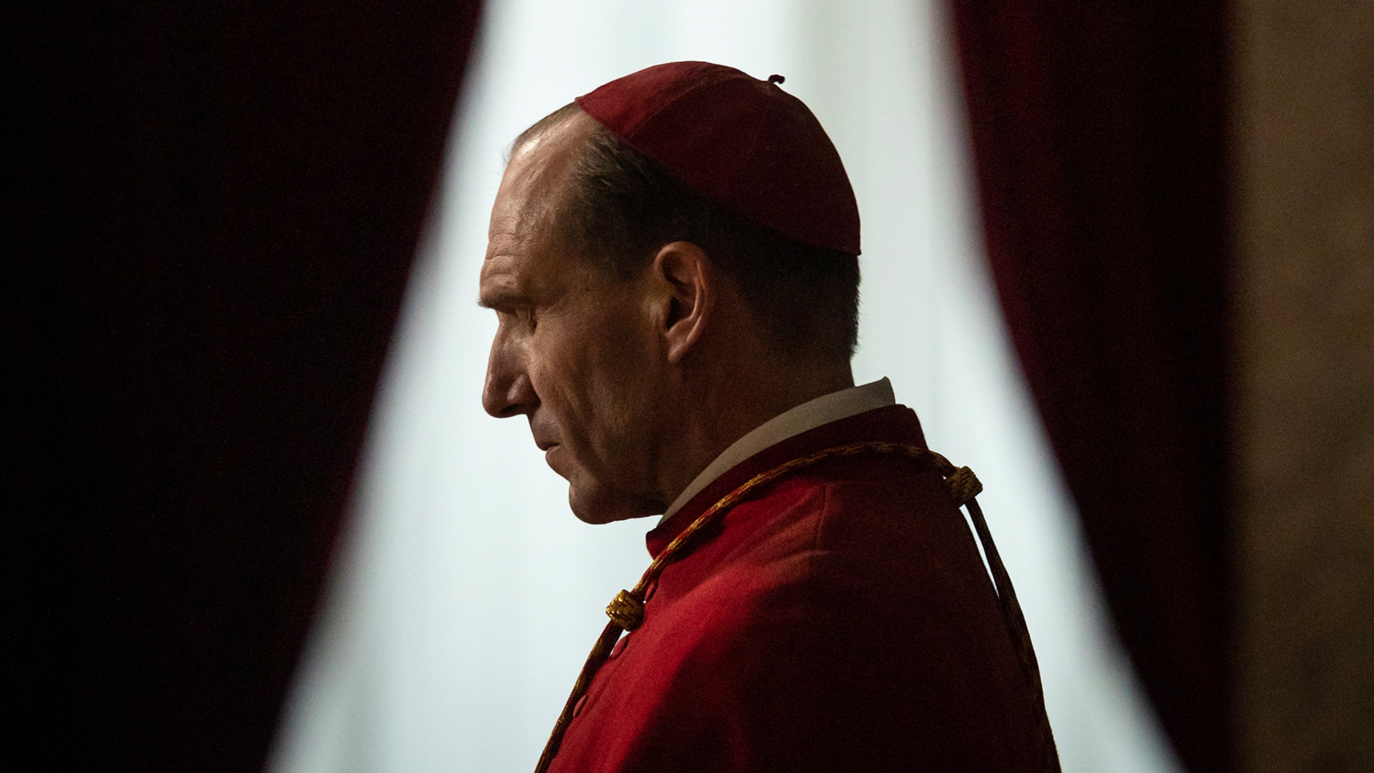 Ralph Fiennes wears a red cap and red robes