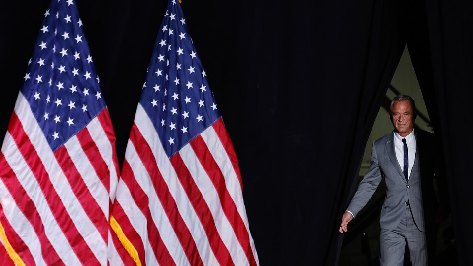 Photo of RFK Jr. walking on stage with two large American flags standing beside him