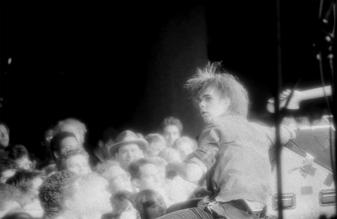 black-and-white concert photo of Nick Cave on stage looking out over crowd