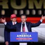 Donald Trump stands behind Mehmet Oz as Oz speaks at a podium