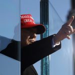 Donald Trump points his finger, and it reflects in the opposite direction on a pane of glass