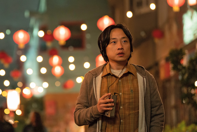 image of Yang from "Interior Chinatown" on street wearing headphones with strings of lantern lights in background