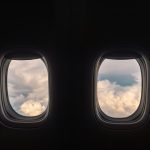 A row of airplane windows show a cloudy sky