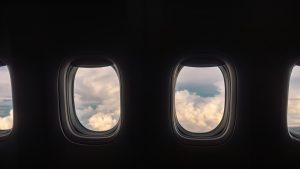 A row of airplane windows show a cloudy sky