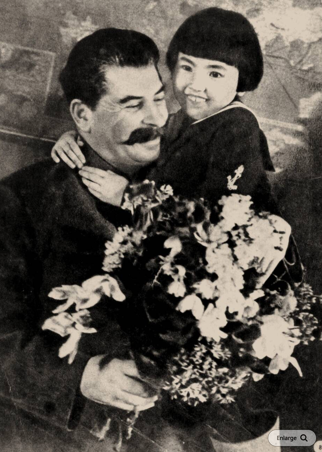 A man with a big mustache has a young girl in his lap while holding flowers.