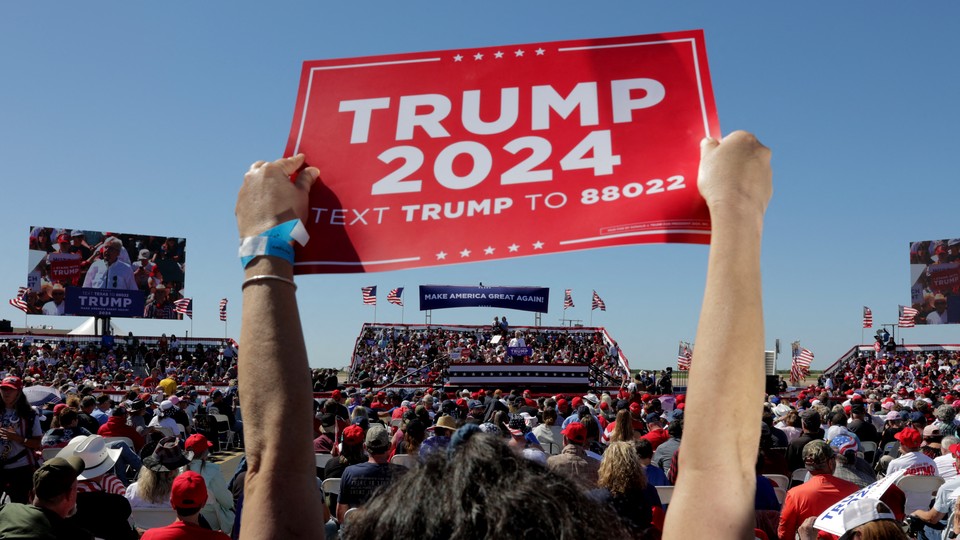 Photo of a "Trump 2024" sign being raised at a Trump rally