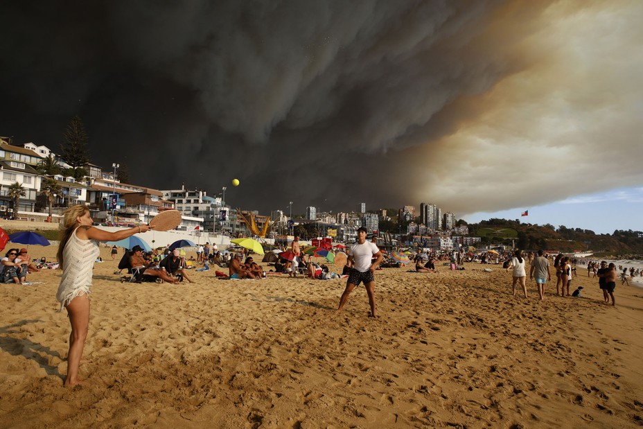 Vacationers play paddleball on a beach backdropped by a darkening sky caused by smoke from nearby forest fires, in Viña del Mar, Chile, on February 2, 2024. Parts of central Chile experienced unusually high temperatures and dry weather, sparking dozens of forest fires that killed more than 100 people.