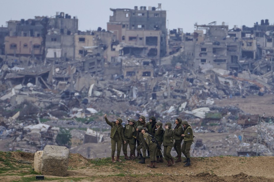 Israeli soldiers pose for a photo on the Gaza Strip border in southern Israel, with destroyed buildings in Gaza seen in the background, on February 19, 2024.