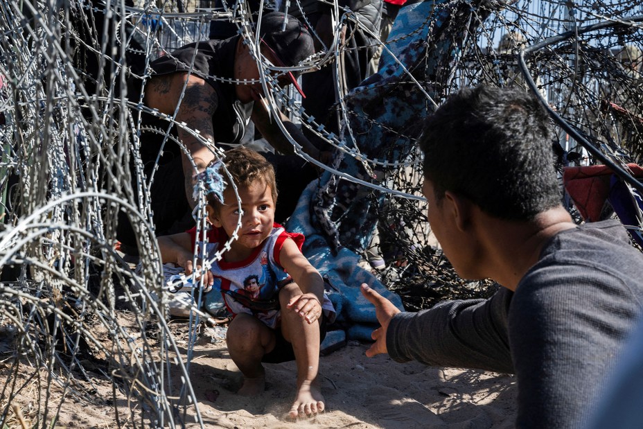 A young boy crawls through a concertina-wire barrier at the border as migrants cross from Mexico into El Paso, Texas, on March 22, 2024.