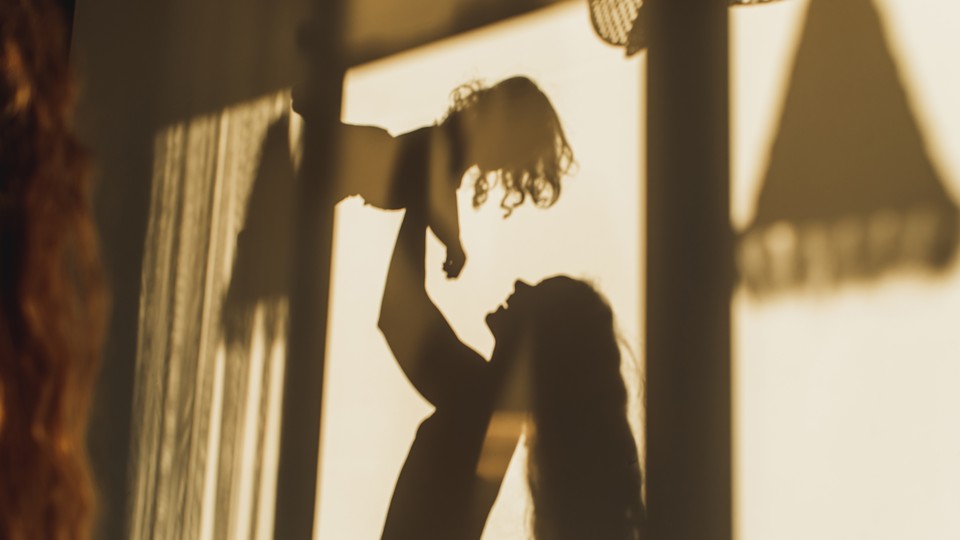 A photograph of shadows on wall of mom playing with her daughter, framed by windows