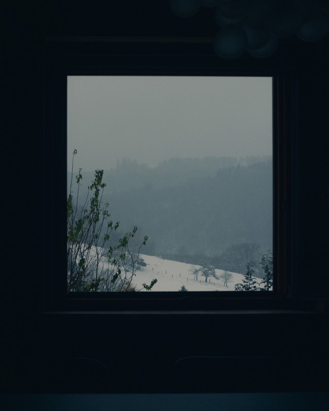 a window in the dark looks out onto a snowy landscape