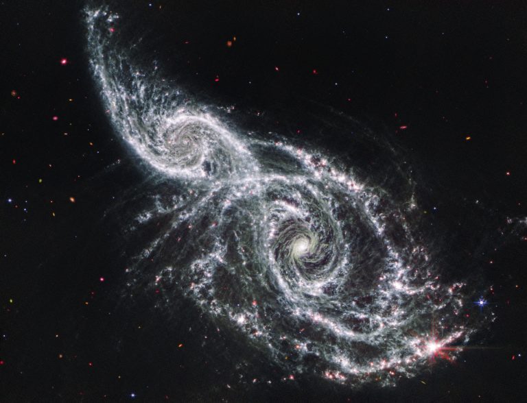 Two spiral galaxies take up almost the entire view and appear to be overlapping. The background of space is black, dotted with tiny foreground stars and extremely distant galaxies.