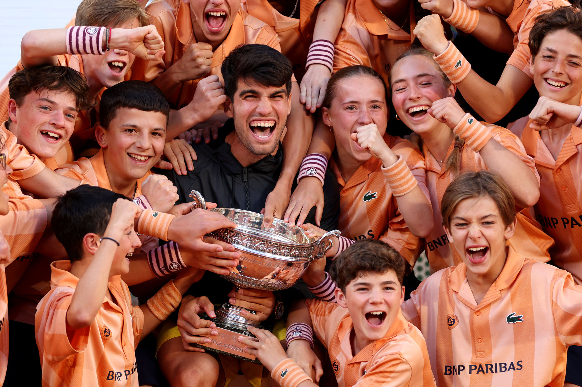 Carlos Alcaraz of Spain holds a French Open trophy as he celebrates with a group of ball kids