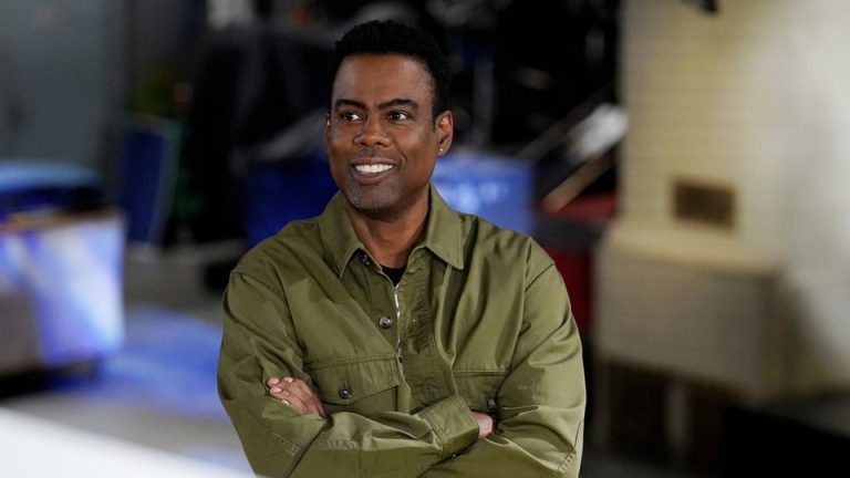 Comedian Chris Rock smiles and looks to the left, with his arms crossed.