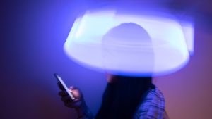 An Asian girl looks at her phone screen with a blurry light distortion around her head