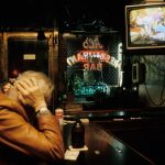 An old man holds his head watching the TV at a bar alone