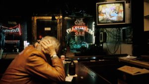 An old man holds his head watching the TV at a bar alone