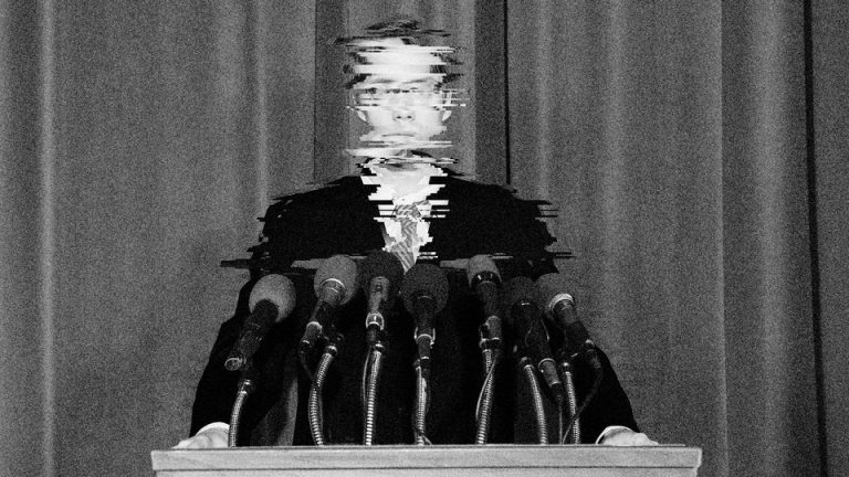 A white man in a suit stands on a podium, with his image so chopped up as to be uncrecognizable