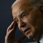 A photo of Joe Biden touching his temple with one hand during his remarks