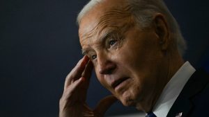 A photo of Joe Biden touching his temple with one hand during his remarks