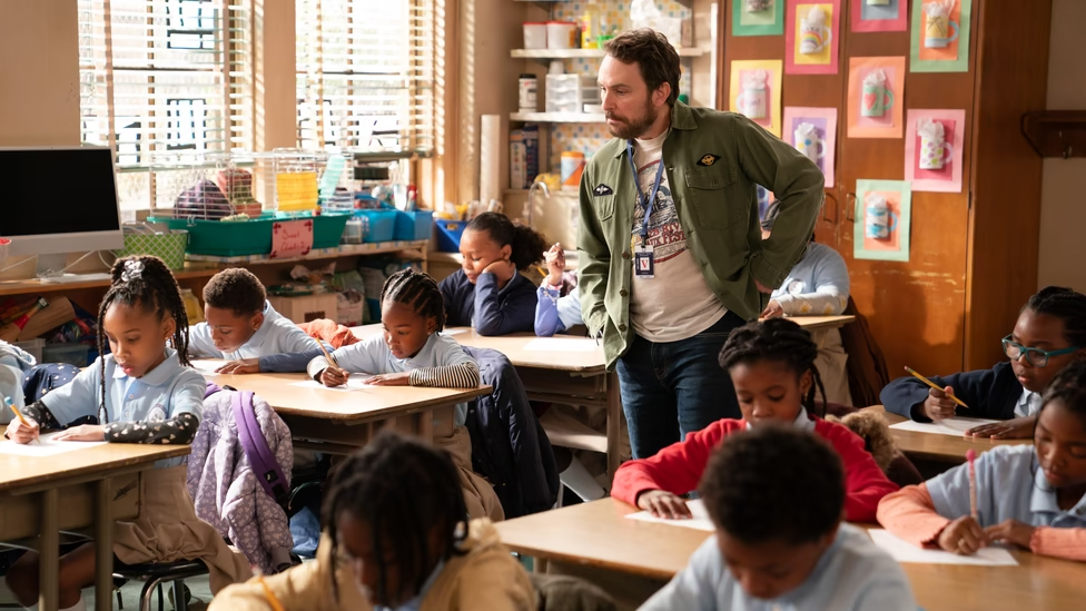 Charlie from It's Always Sunny in Philadelphia stands in an Abbott Elementary classroom