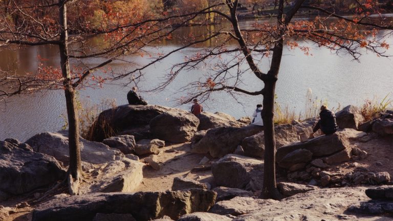 photo of people sitting on rocks next to water with fall foliage